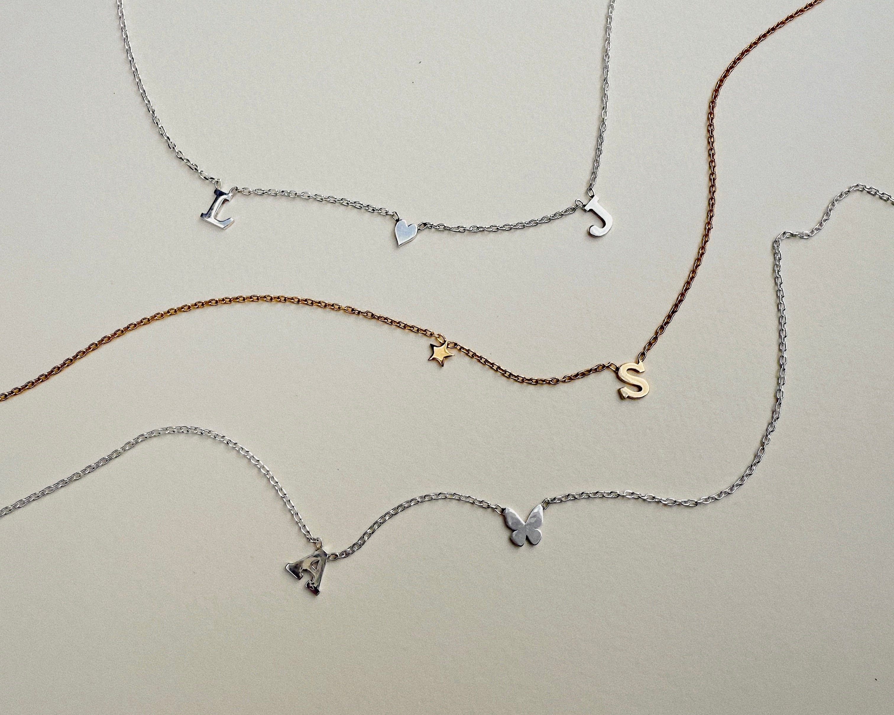 Set of four initial necklaces with various charms on a light gray background