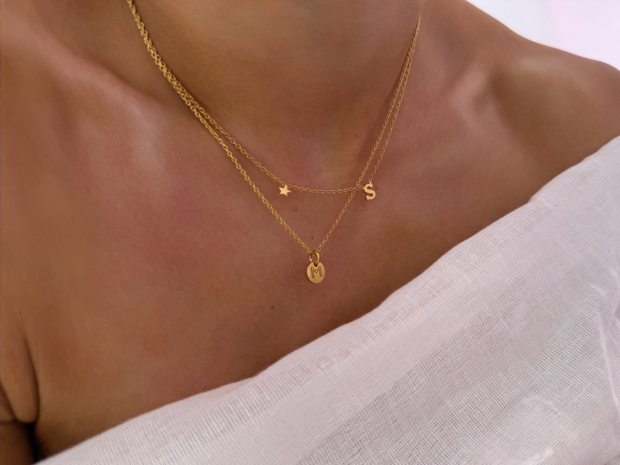 Close-up of a person wearing a gold necklace with small pendants on a light background