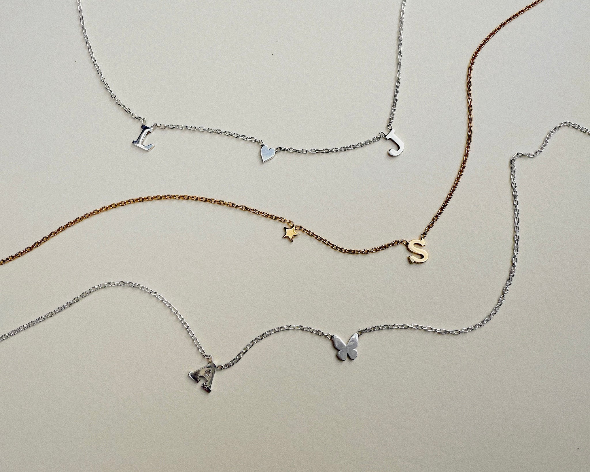 Set of four initial necklaces with various charms on a light gray background