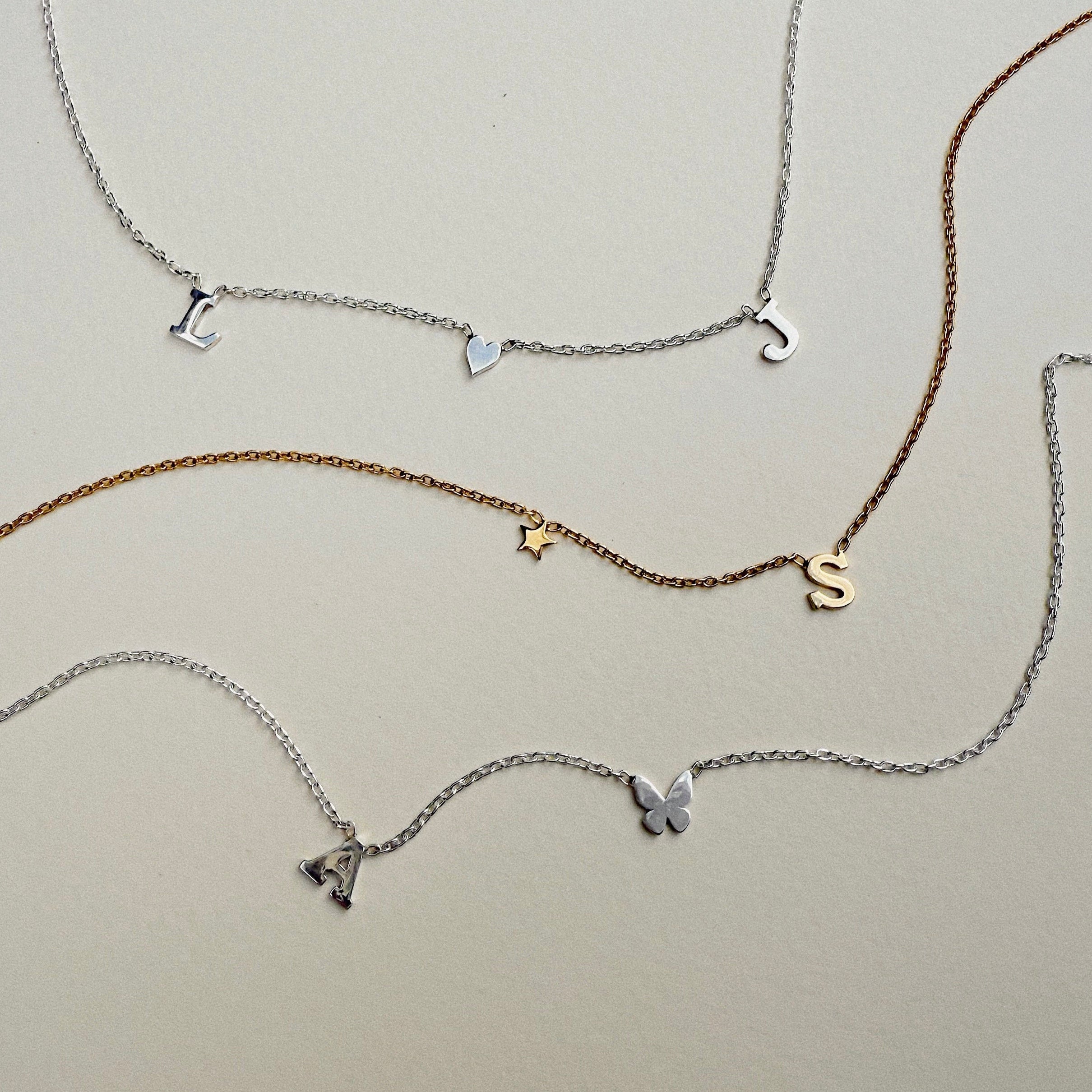 Set of four initial necklaces with various charms on a light gray background