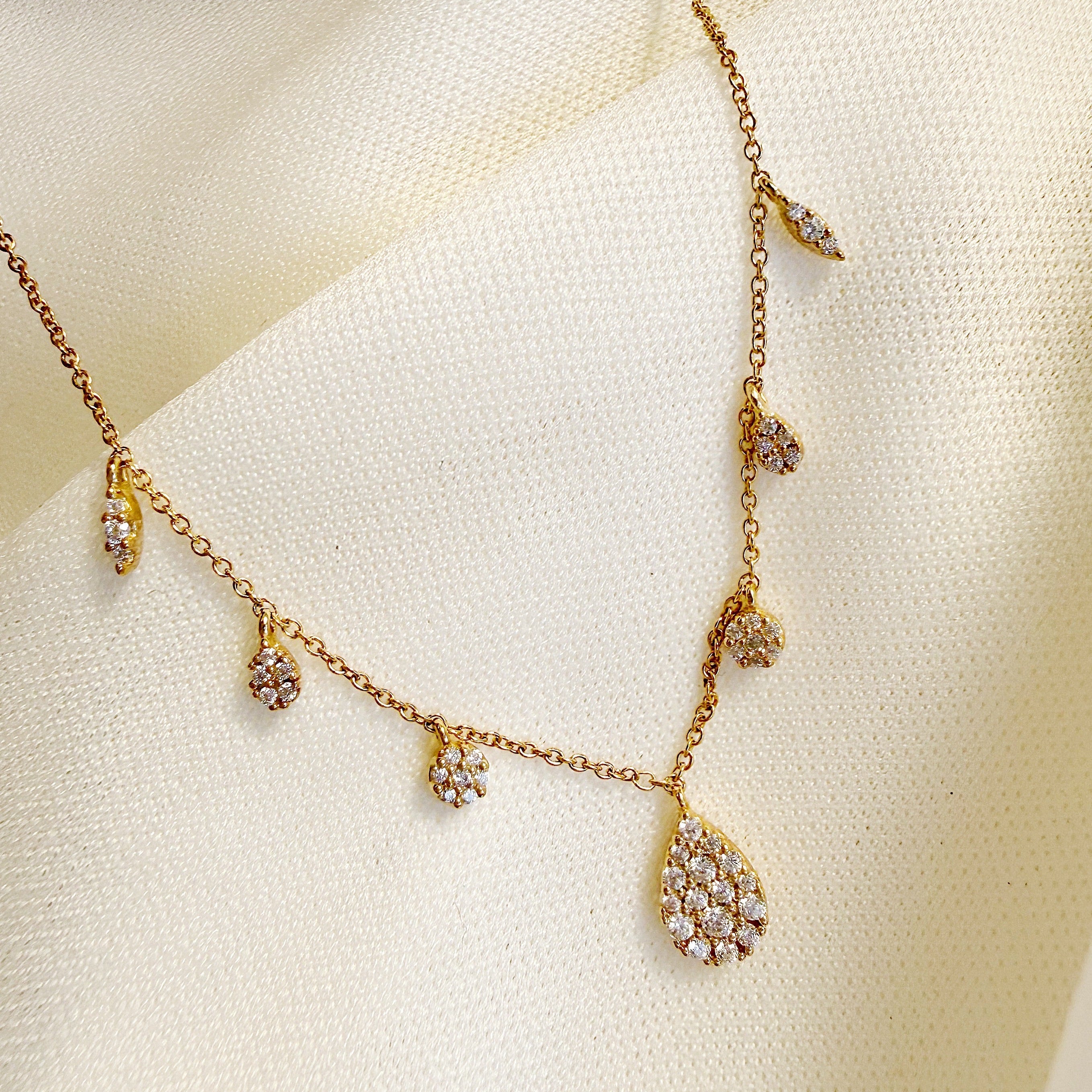 Gold necklace with teardrop-shaped pendants on a soft beige fabric background