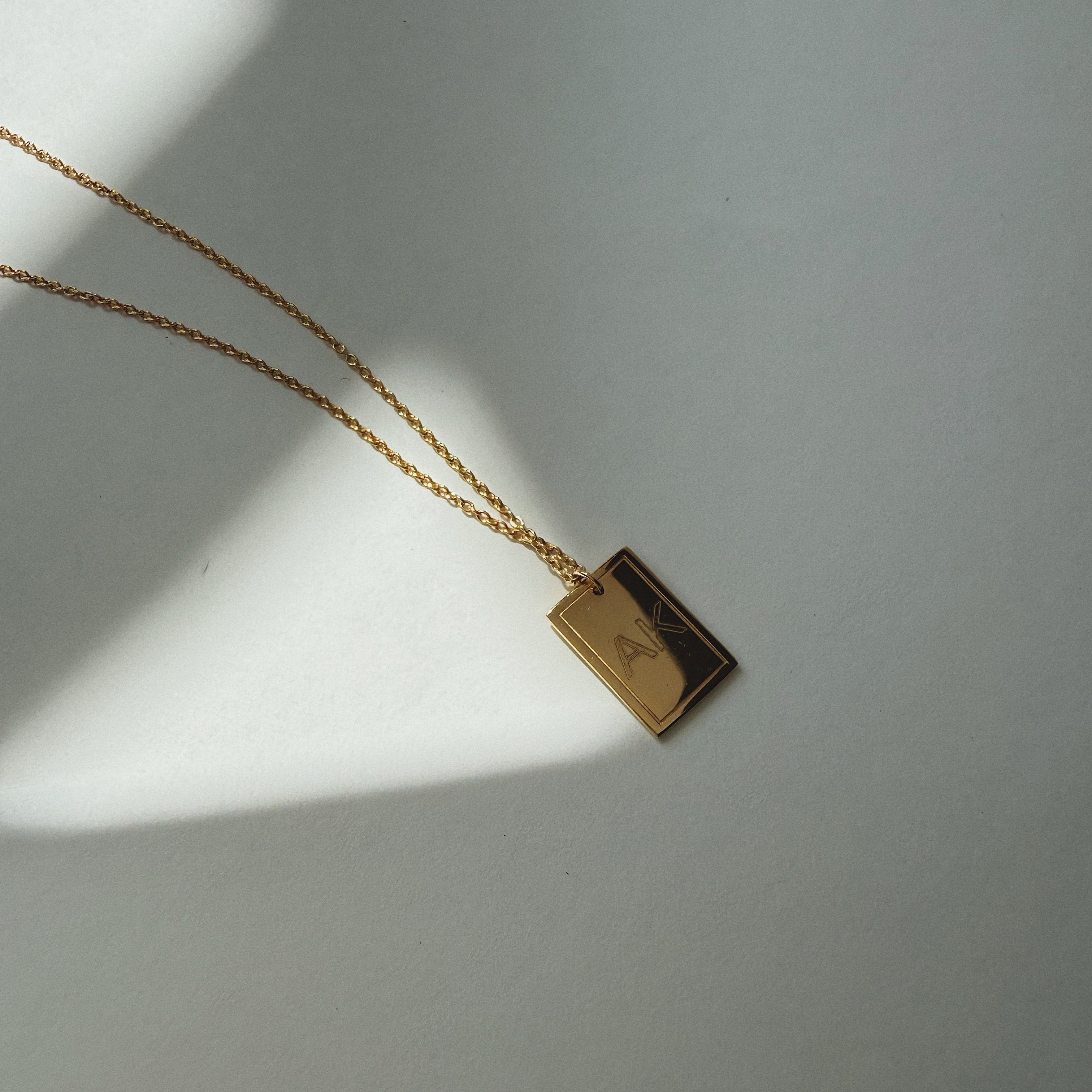 Gold necklace with a rectangular pendant on a light gray background