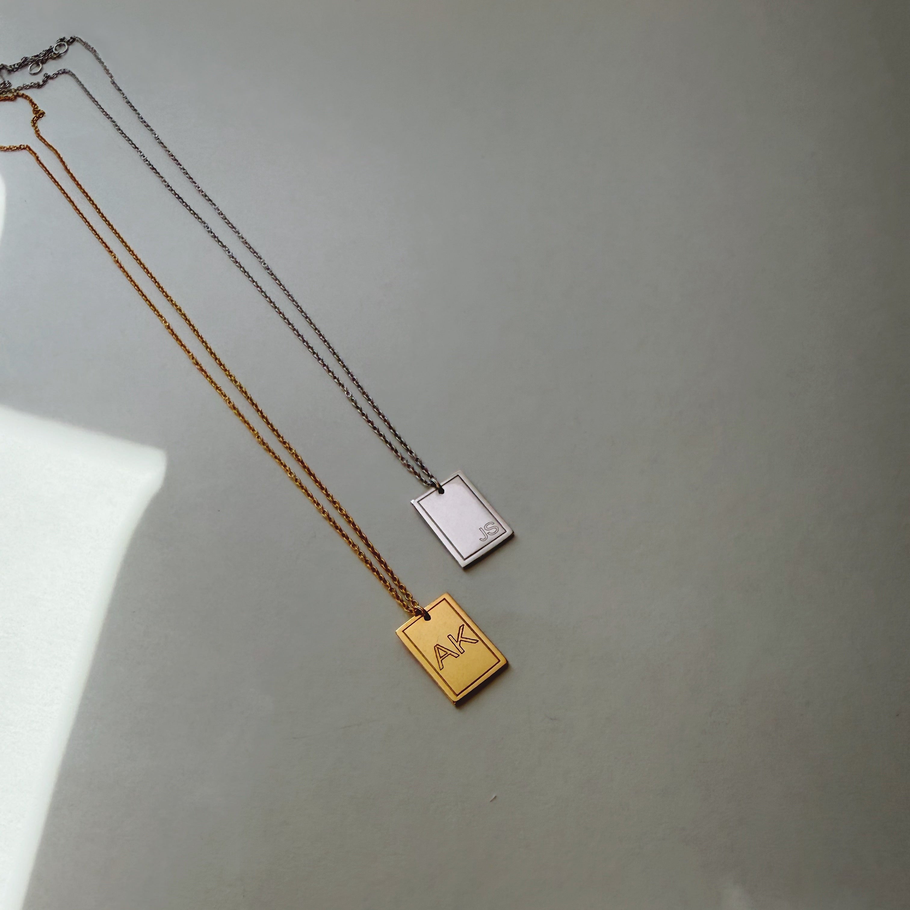 Two necklaces with rectangular pendants on a light gray background